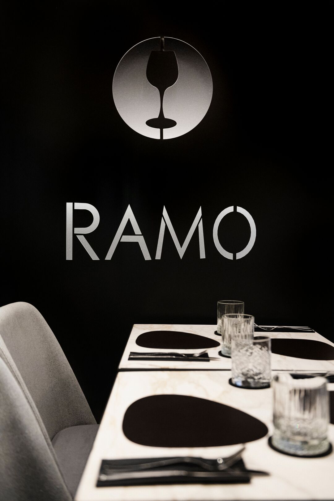 La parete nera del Ramo Bistrot con il logo: un calice dentro un cerchio e la scritta RAMO, sopra un tavolo in marmo apparecchiato